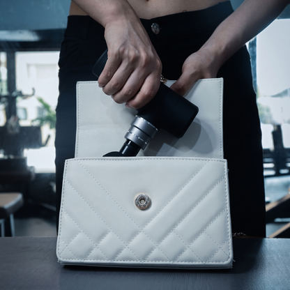 Mini Percussion Massager being slipped into a small white handbag, showing how little room it takes