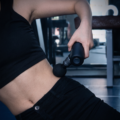 Mini Percussion Massager held against the hip while sitting in a gym, ball head fitted